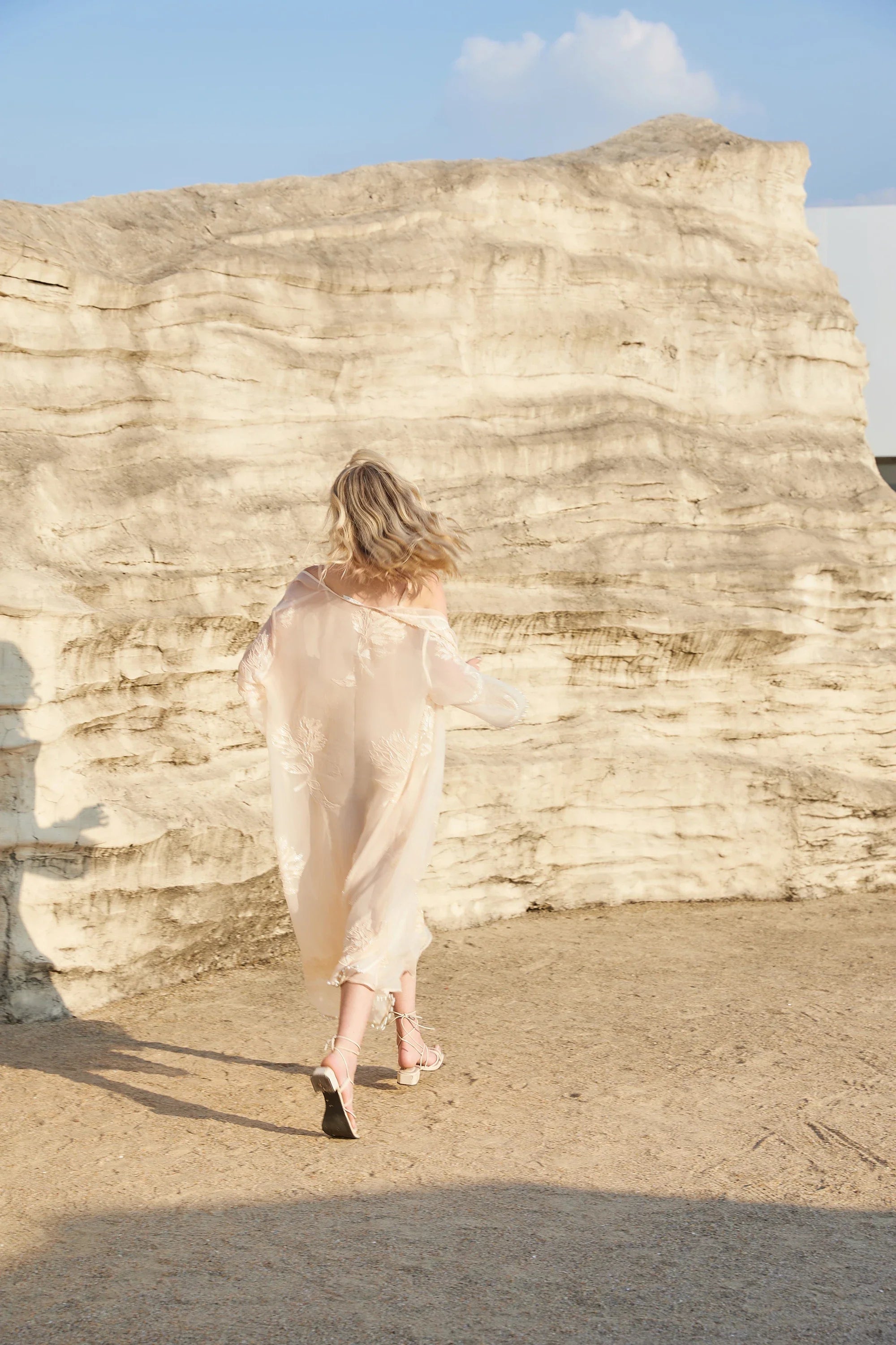 Back outdoor view of the Elppis blush pink sheer midi slip dress